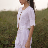 Woman in a white linen outfit standing in a grassy field.
