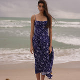Woman in a blue patterned dress standing on a beach with ocean waves in the background