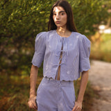 Woman wearing a light blue outfit standing in a natural setting with greenery.