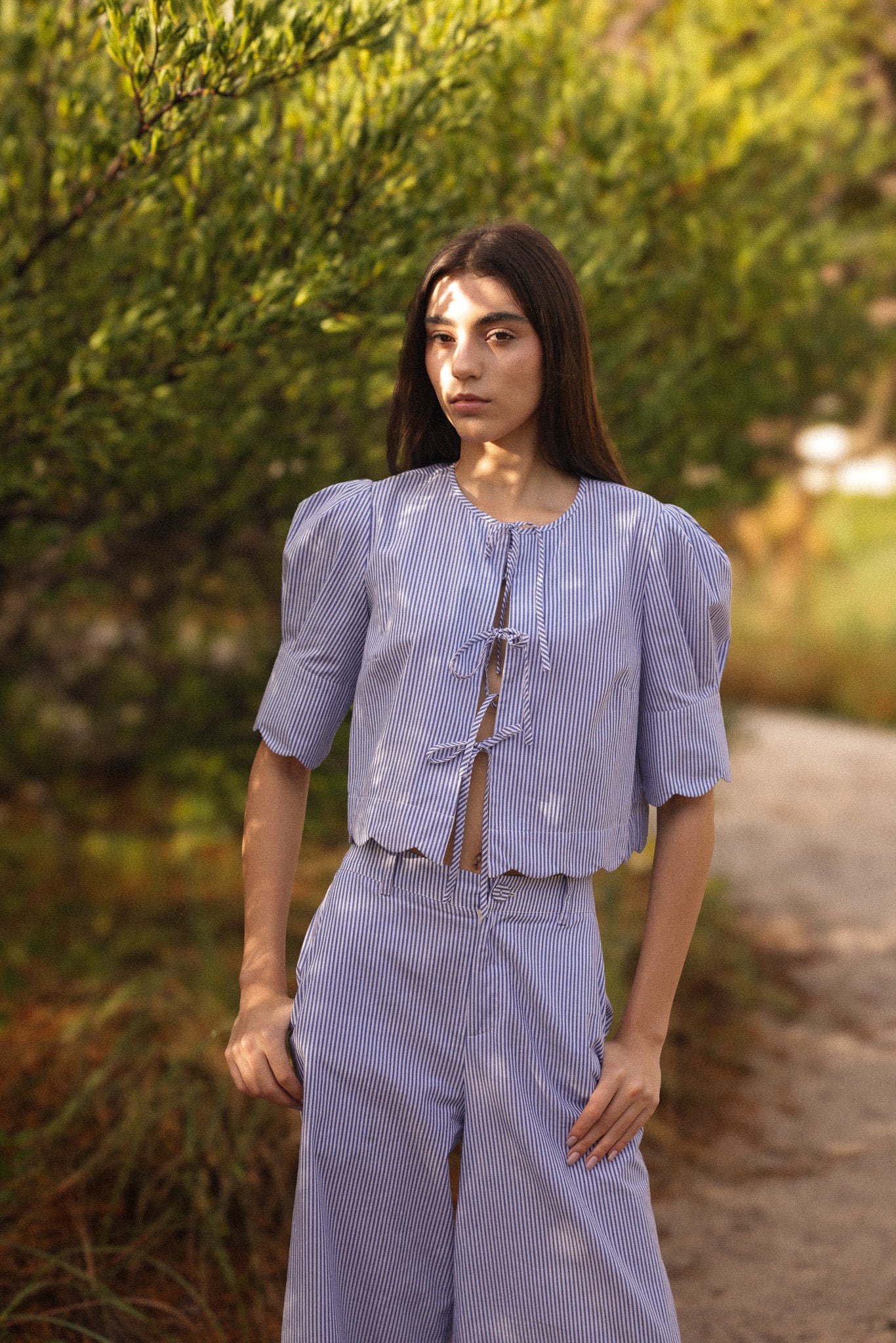 Woman wearing a light blue outfit standing in a natural setting with greenery.