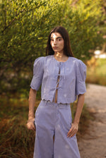 Woman wearing a light blue outfit standing in a natural setting with greenery.