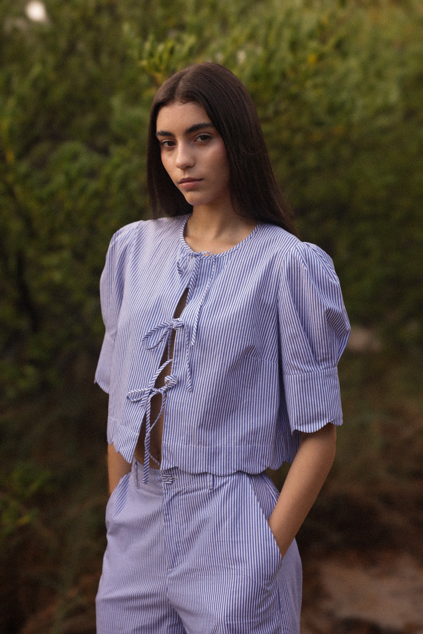 Woman wearing a blue striped outfit standing outdoors with greenery in the background