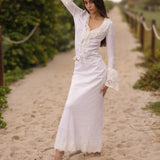 Woman in a white dress standing on a sandy path with greenery around.