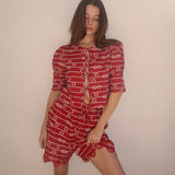Woman wearing a red dress with white patterns against a plain background