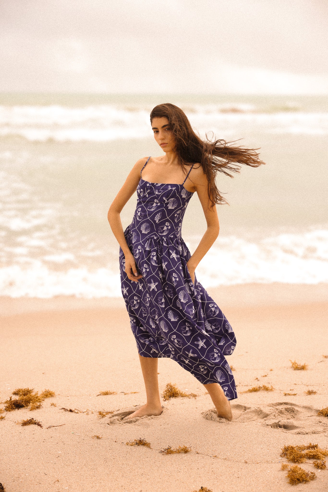 Woman in a purple dress standing on a beach with waves in the background
