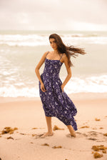 Woman in a purple dress standing on a beach with waves in the background