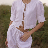 Model wearing a white linen tie-front top with matching eyelet shorts, styled for an effortless coastal summer look by Sister New York.