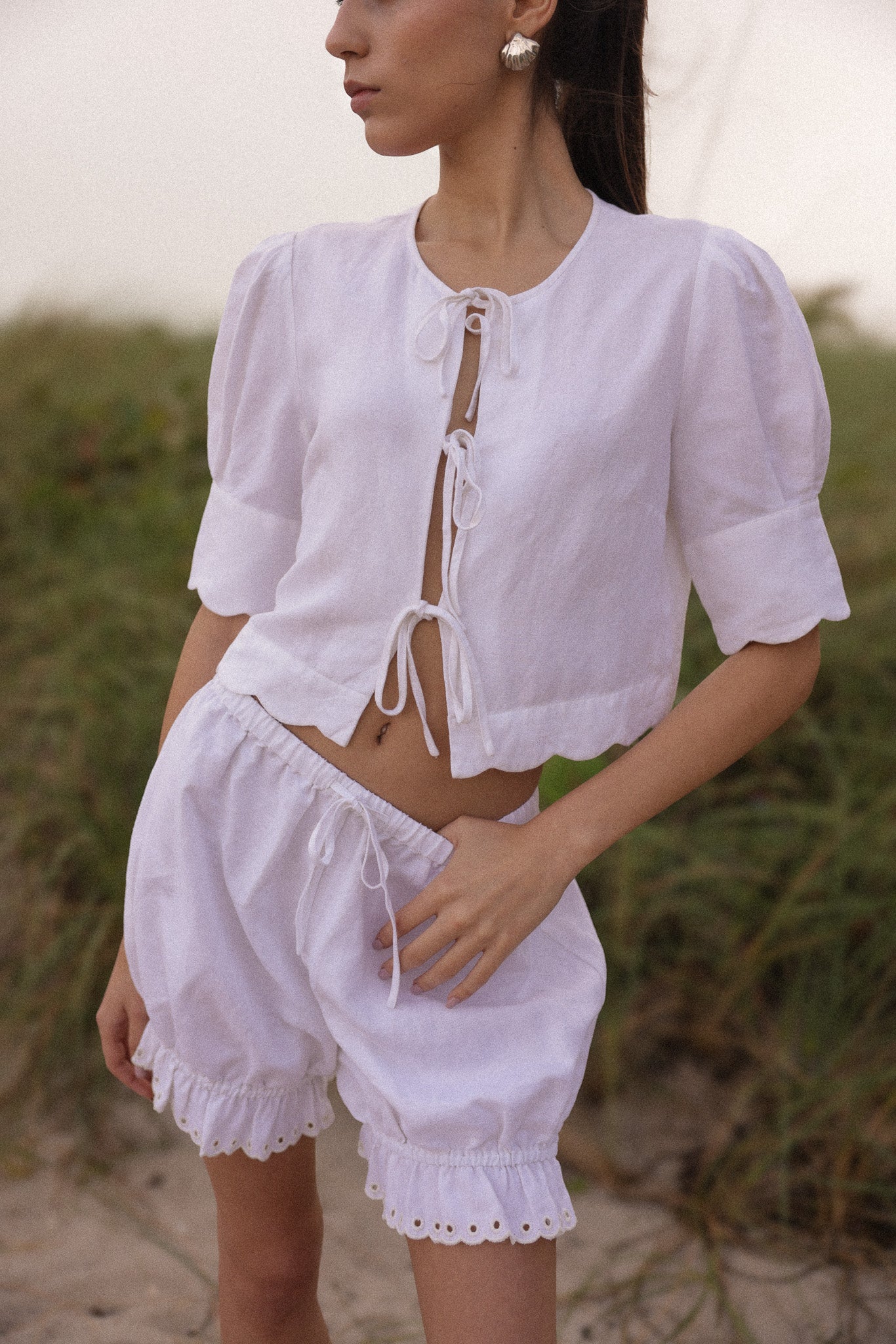 Model wearing a white linen tie-front top with matching eyelet shorts, styled for an effortless coastal summer look by Sister New York.