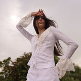  Model wearing a white linen tie-front top with lace bell sleeves, styled for an elevated summer resort look by Sister New York.